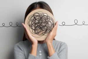 Person holding a round wooden board with a tangled black scribble over their face, symbolising the hidden and complex effects of trauma.