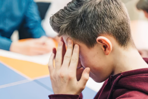 Child sitting in a classroom with their head in their hands, showing signs of school anxiety and distress.