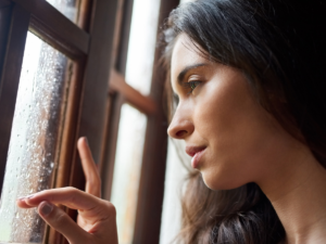 Woman looking out of a rainy window during darker autumn weather